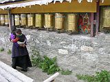 Tibet Kailash 02 Nyalam 09 Gompa Pilgrim with Baby A few devout Buddhist women circumambulated the Nyalam gompa, spinning the prayer wheels and saying mantras. Here is a mother carrying her baby on her back. Notice the nicely painted stone among the mani wheels.